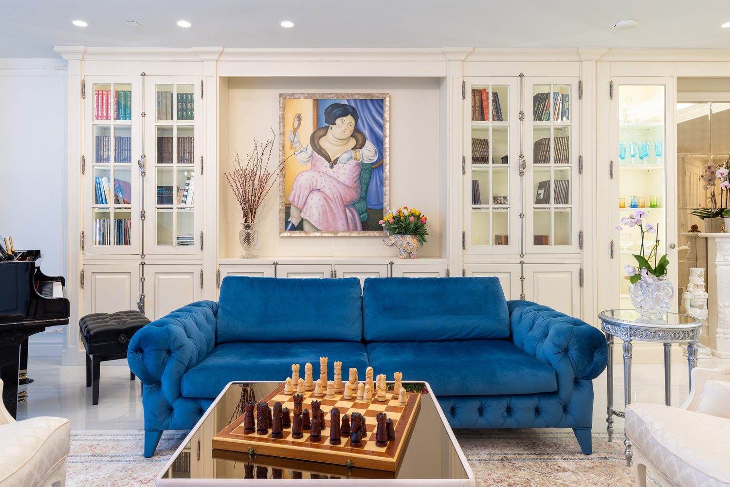 Living room with commissioned cream cabinetry, blue velvet sofa, grand piano and framed artwork